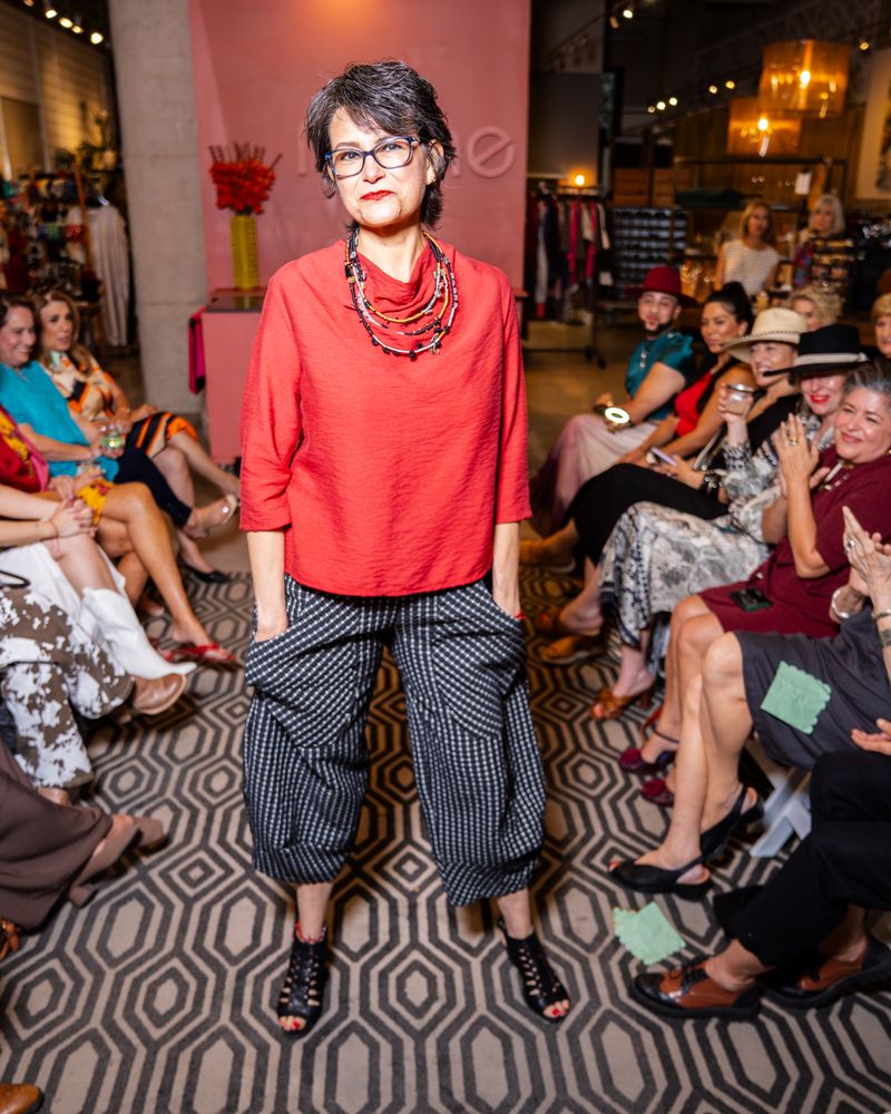 model in a red cowl top, layered necklace and patterned pants on a runway