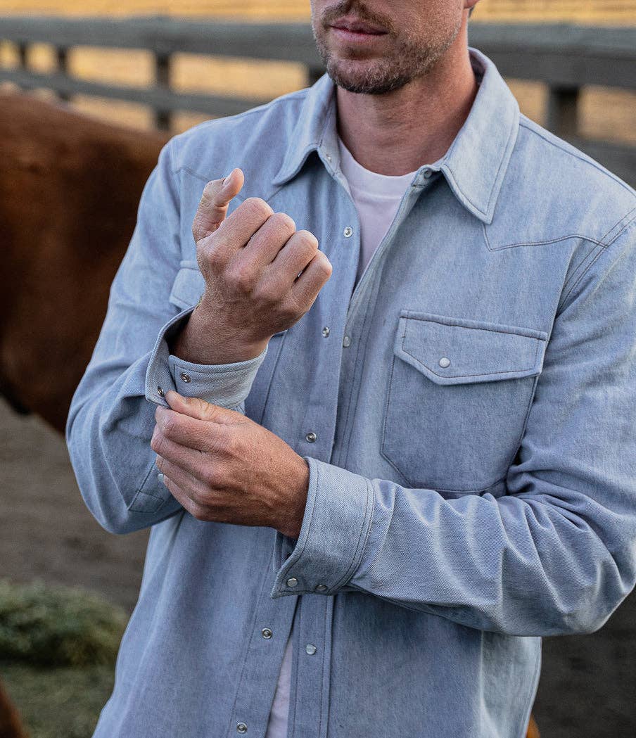 Man wearing a light blue denim shirt with a horse in the background