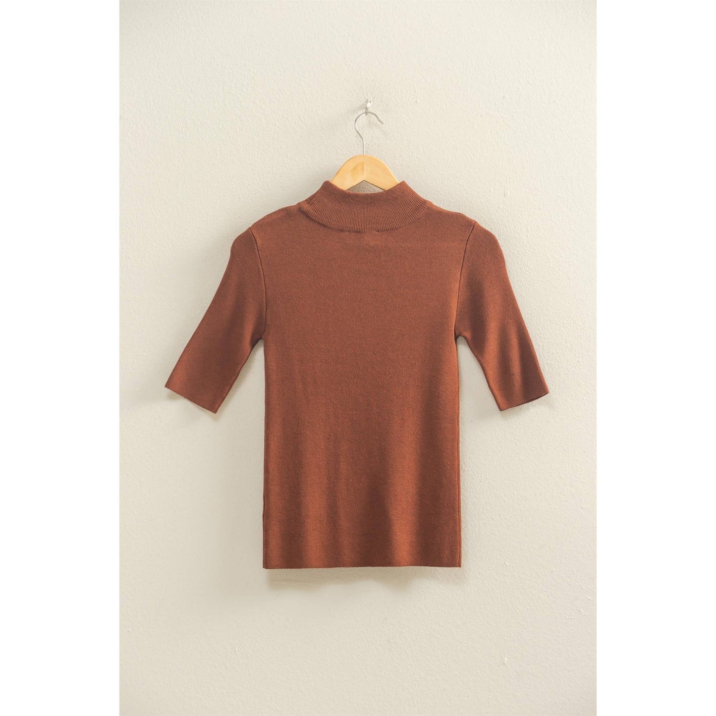 brown mock neck half sleeve top on a hanger against a beige wall