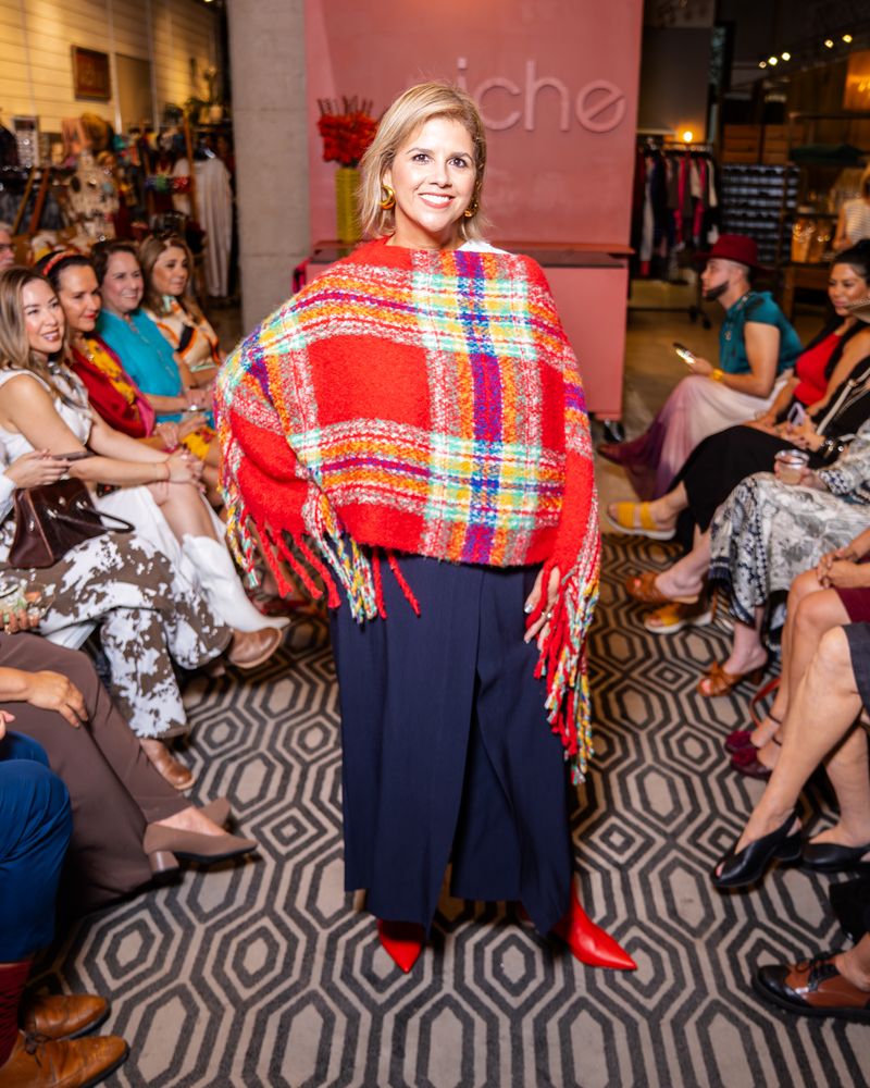 model wearing a red plaid poncho, navy pants and red boots on a runway