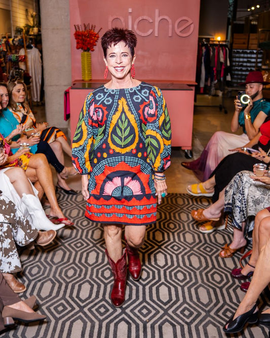 model in a colorful embroidered dress and red boots walking down runway