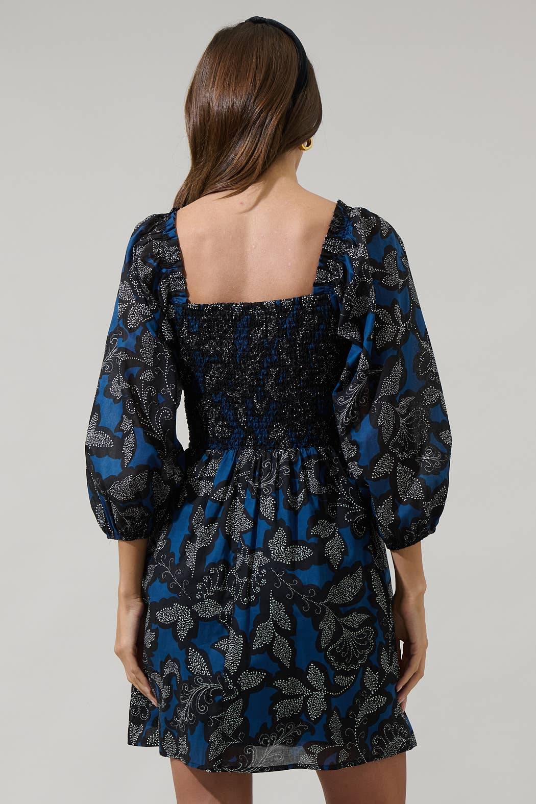 Woman wearing a black and blue floral dress with long sleeves on a gray background