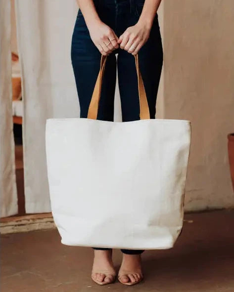 Person holding a white tote bag with brown handles indoors.