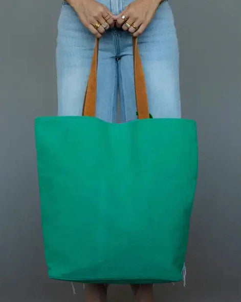 Person holding a teal tote bag with brown handles against a gray background