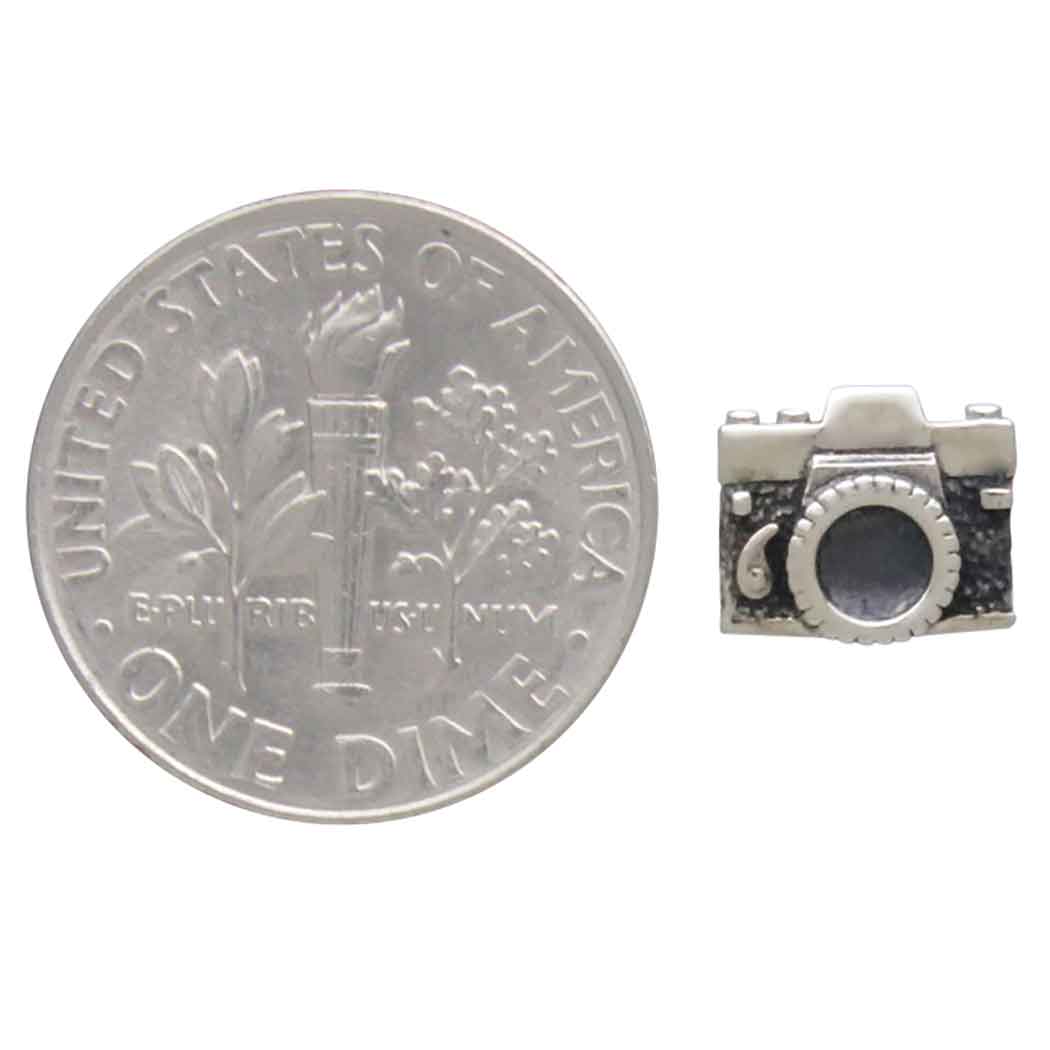 Silver camera charm next to a U.S. dime on a white background