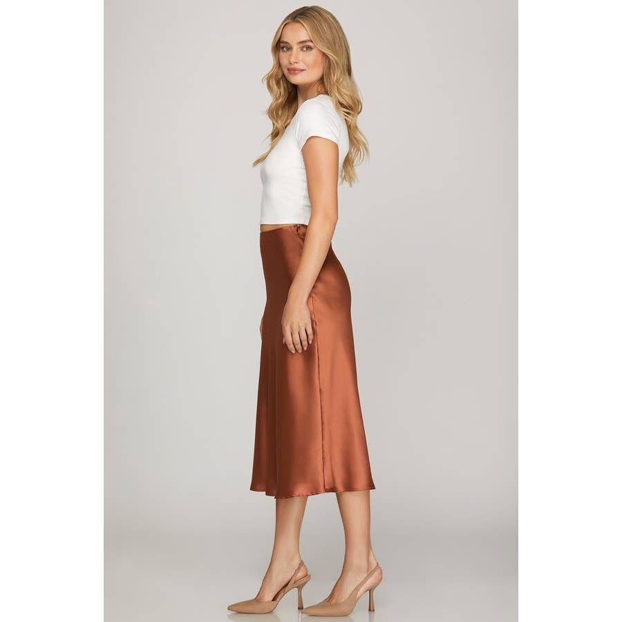 Woman wearing a white top and copper satin skirt on a plain background