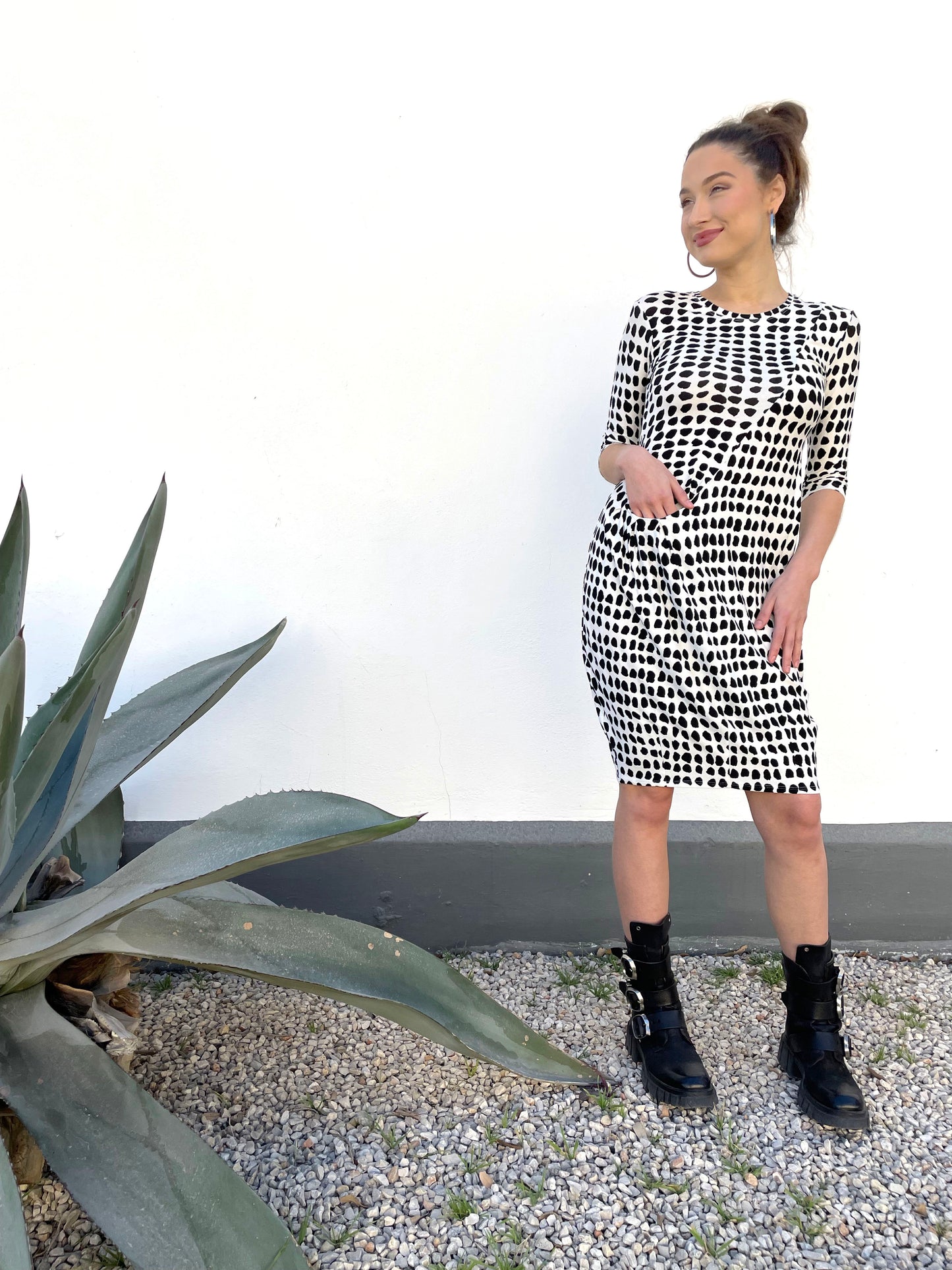 model in a white pullover tunic with a black dot print. dress has an asymmetrical seam across the front body with a curved pocket set into a seam at the hip. dress is knee lengh and has 3/4 sleeves and a round neckline