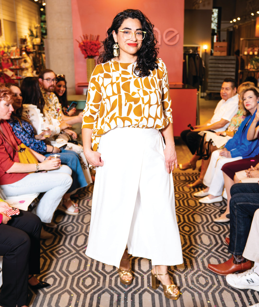 model in a wide leg white pant with an overlapping panel on both legs, crossing in the front. worn with a brown and white mod print top with 3/4 sleeves