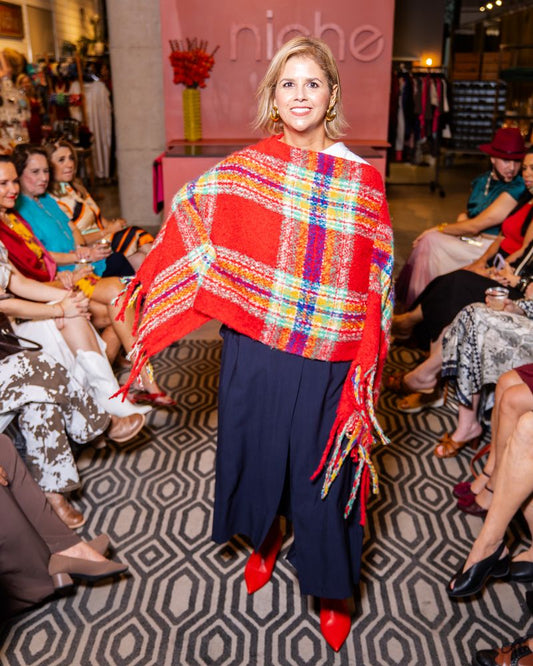 model wearing a red plaid poncho, navy pants and red boots on a runway