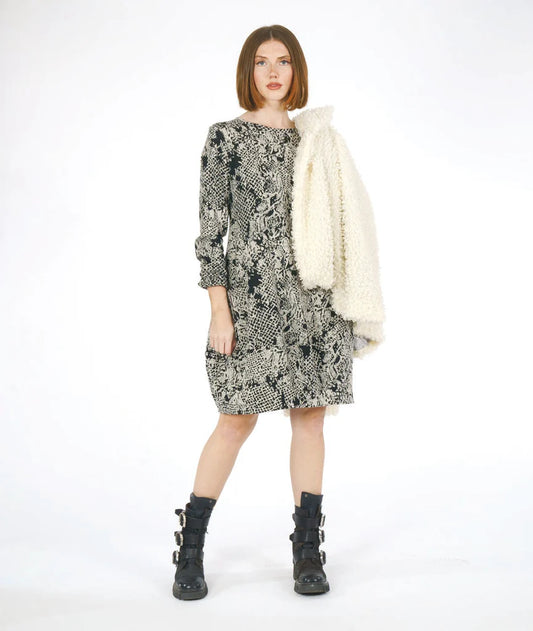 model wearing a patterned dress with long sleeves and a fuzzy coat on her shoulder on a white background