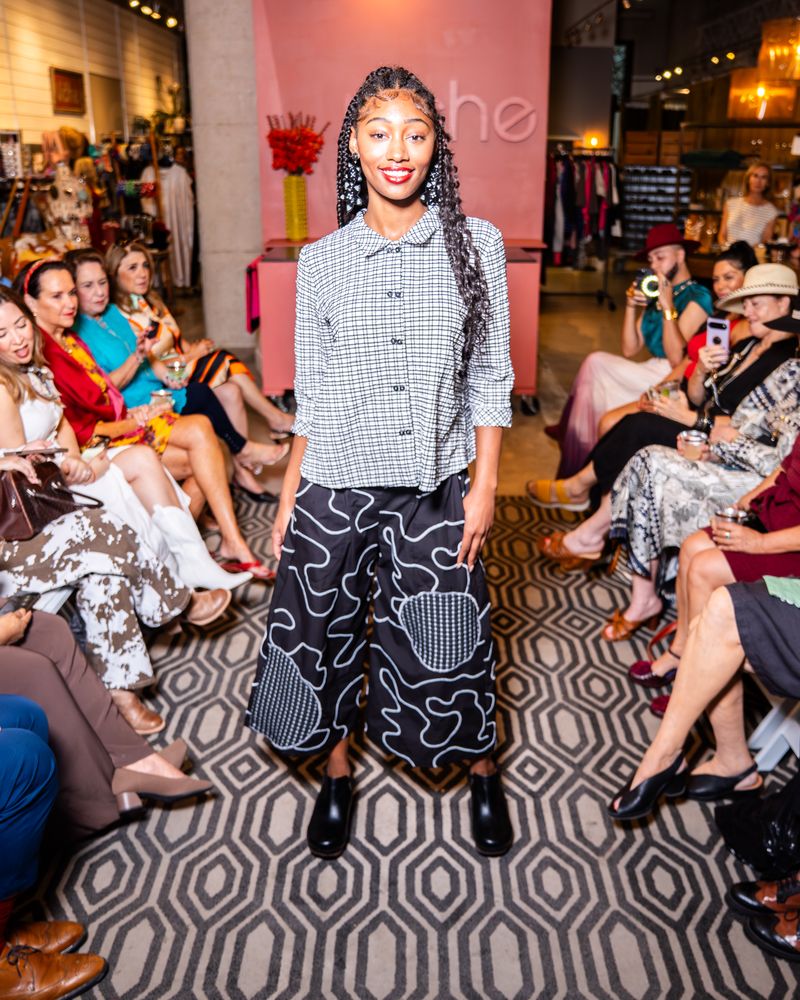 model posing in a checkered button up top and swirl pattern pants on a runway