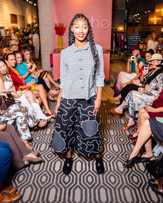 model posing in a checkered button up top and swirl pattern pants on a runway