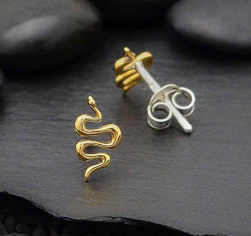 shiny bronze earrings in shape of a windy snake. against a dark slate background with pebbles