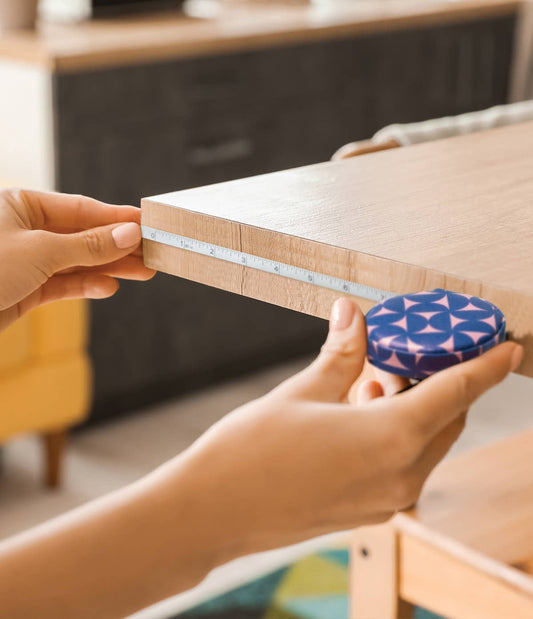 2 hands holding a tape measurer against a wooden shelf