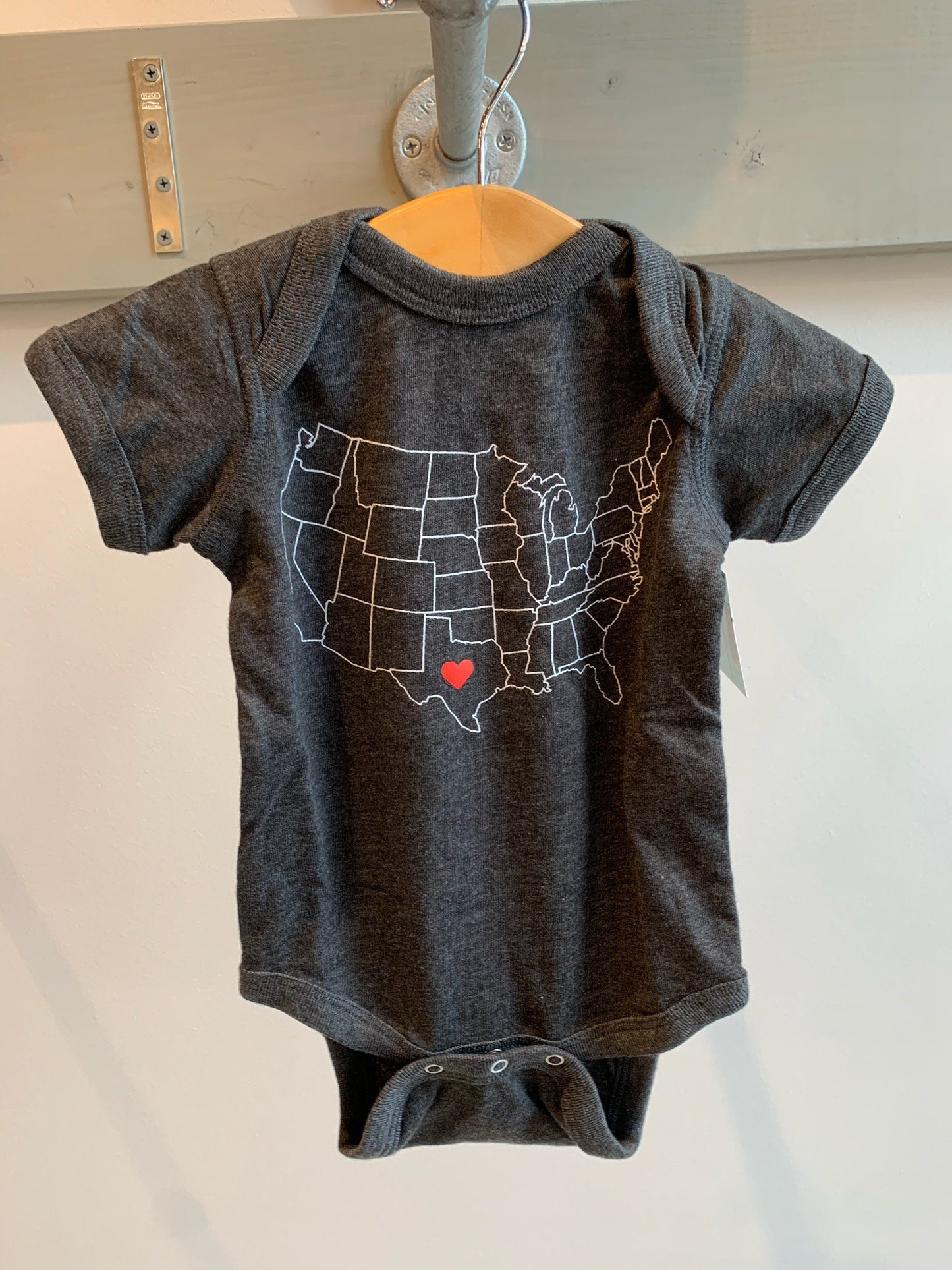 a dark grey baby onesie with a drawing of  the united states with a heart in the center of texas