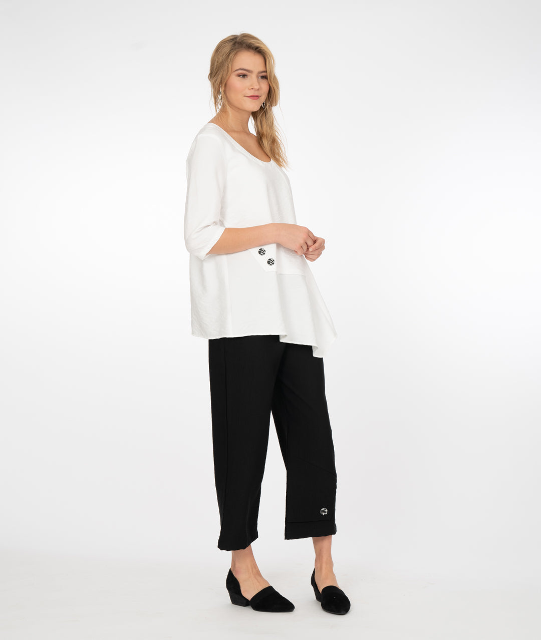 blonde model wearing a white top with black pants both with button detail in front of a white background