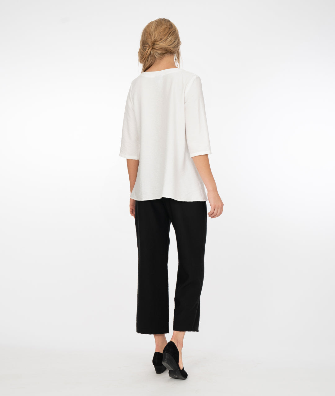 blonde model wearing a white top with black pants both with button detail in front of a white background