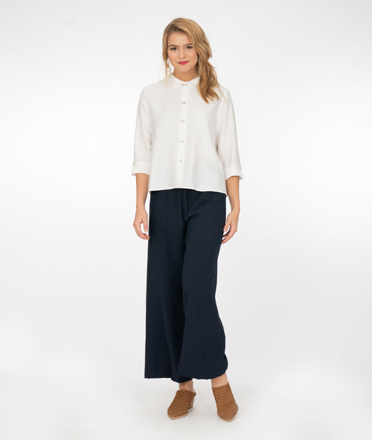 blonde model wearing a white button up shirt with navy blue pants in front of a white background