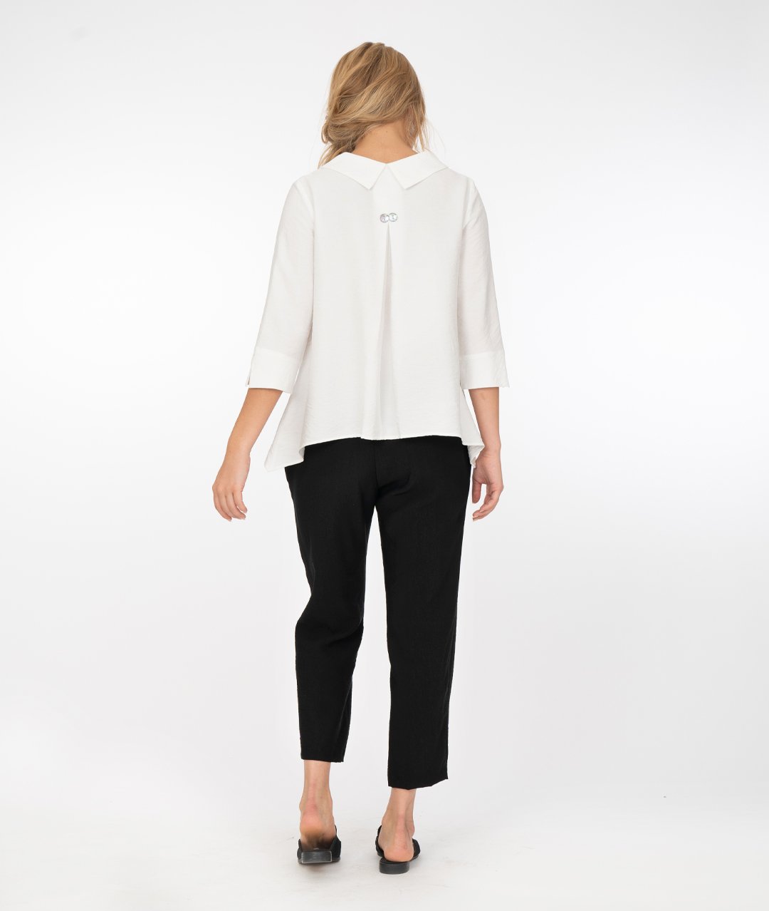 model in a white button up jacket with a collar and splits at the cuffs of the sleeves. Wearing black pants and shoes, standing in front of a white background
