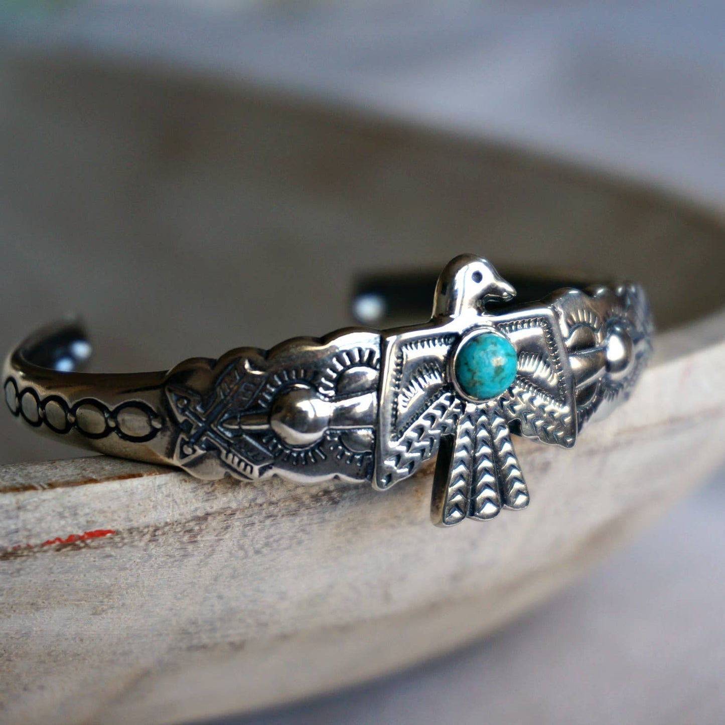 Slim detailed Sterling silver cuff w/ Thunderbird design and one Turquoise stone inlay set against a grey background
