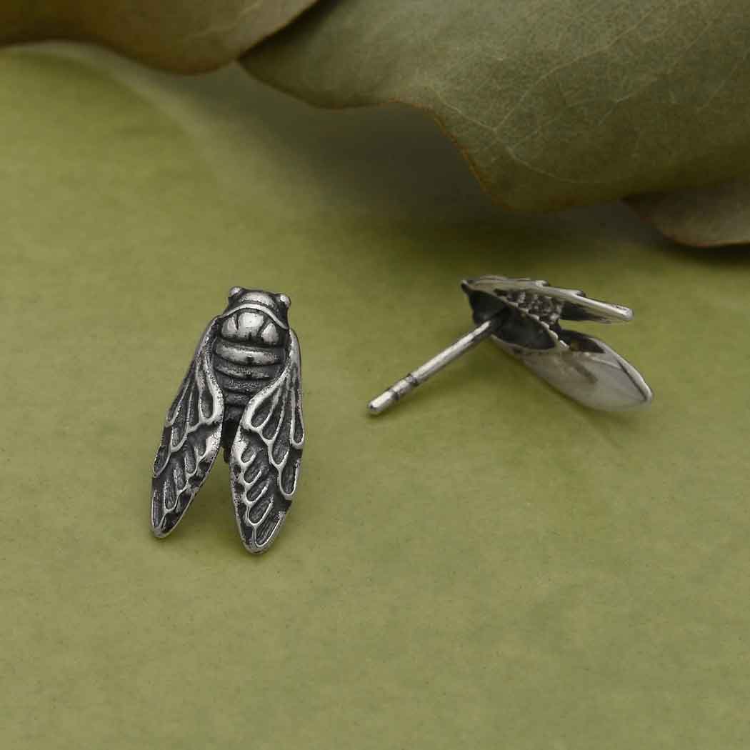 A pair of sterling silver earrings designed to resemble the post of a cicada, with a detailed sculptural pattern.