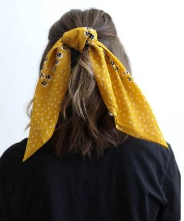 Pictured is the back of a brunette model's head. The model is wearing her hair halfway up with the yellow scarf tied around her hair.