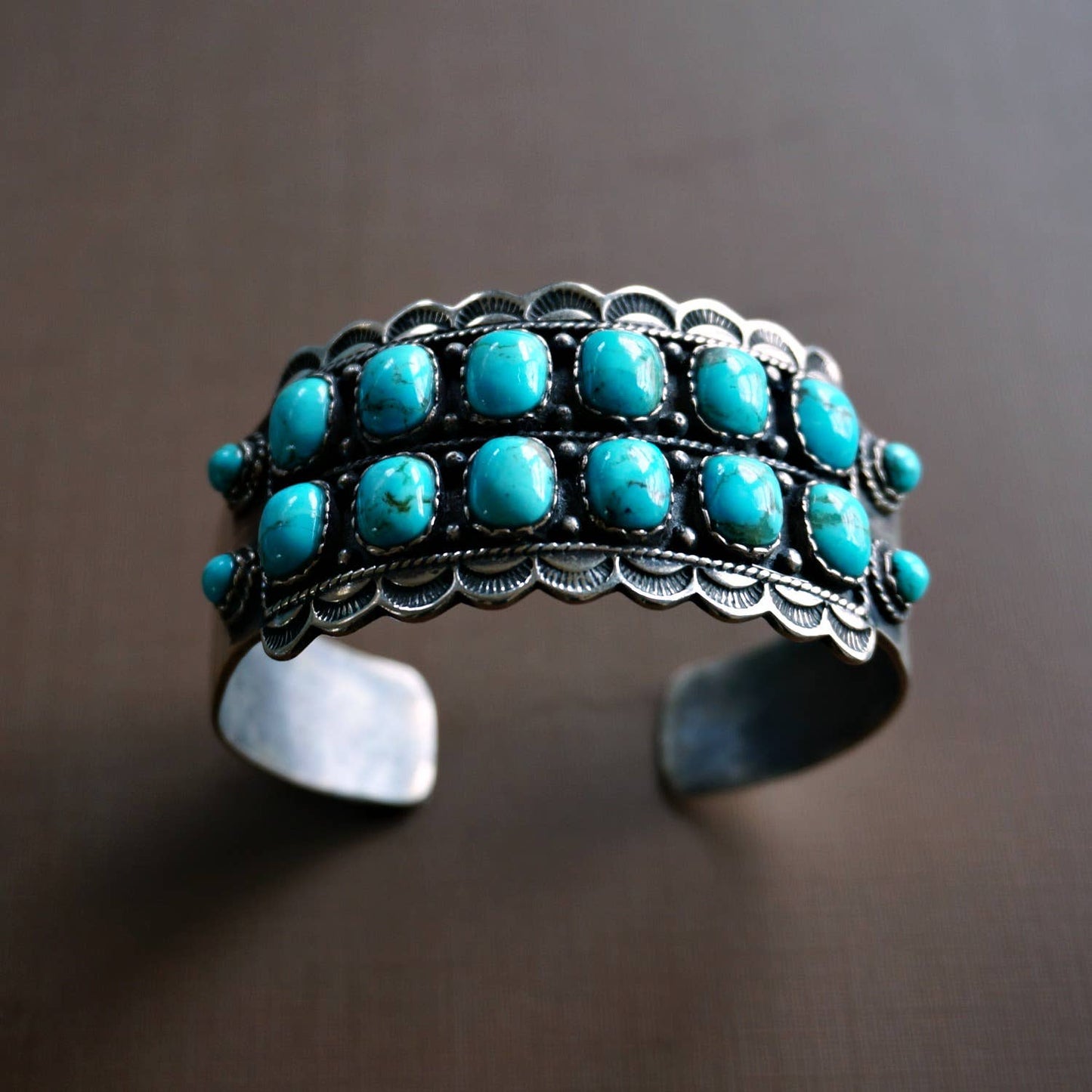 Turqouise and Sterling Silver detail cuff against a brown backkground. Hastwo rows of Turqouise w/ six stones in each row and two addtional smaller stones at both ends of cuff stones