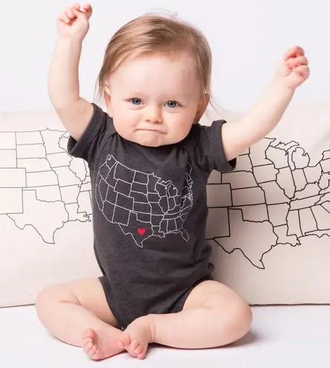 baby in a gray onesie with a map of the united states printed on it in white, with a red heart over texas