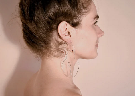 Silver wired earrings in the form a woman's body on the ears of a caucasian model.