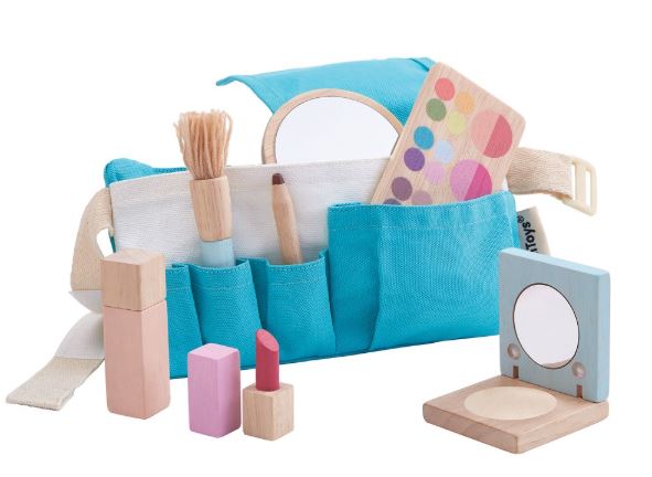 Pictured is a wooden makeup set that features a blue utility belt, pretend makeup palette, mirror, compact, perfume bottle, lipstick, eyeliner, and makeup brush. Pictured against a white background.
