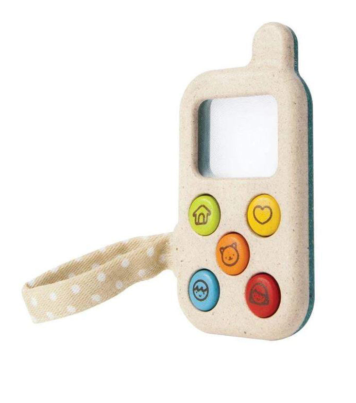 Toy phone made out of wood with a mirrored square as a screen and five buttons on it. There is a green button with a house on it, yellow button with heart on it, orange button with a bear on it, red button with a girl on it, and blue button with a boy on it. There is a beige ribbon attached to it with white polka dots and it is pictured against a white background.