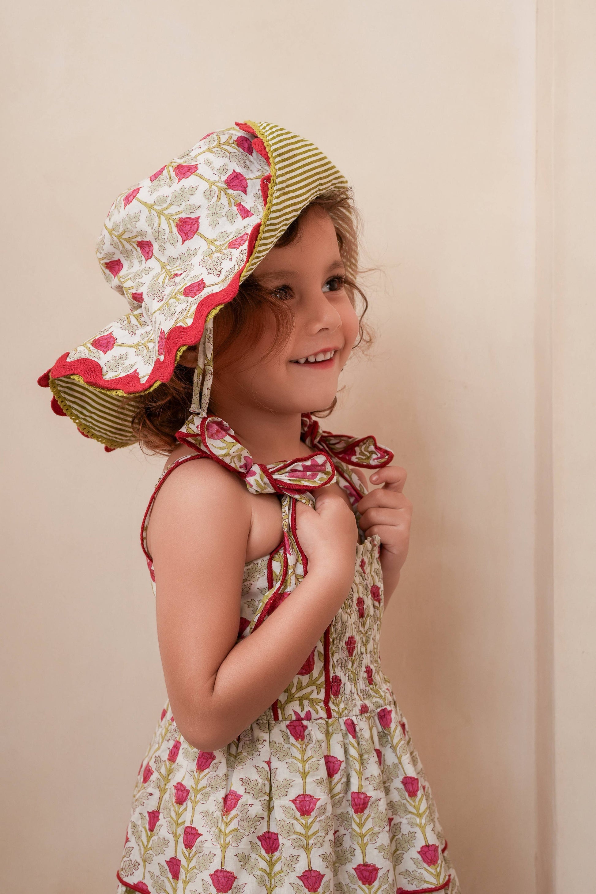 Young girl wearing a floral dress and sun hat against a beige background