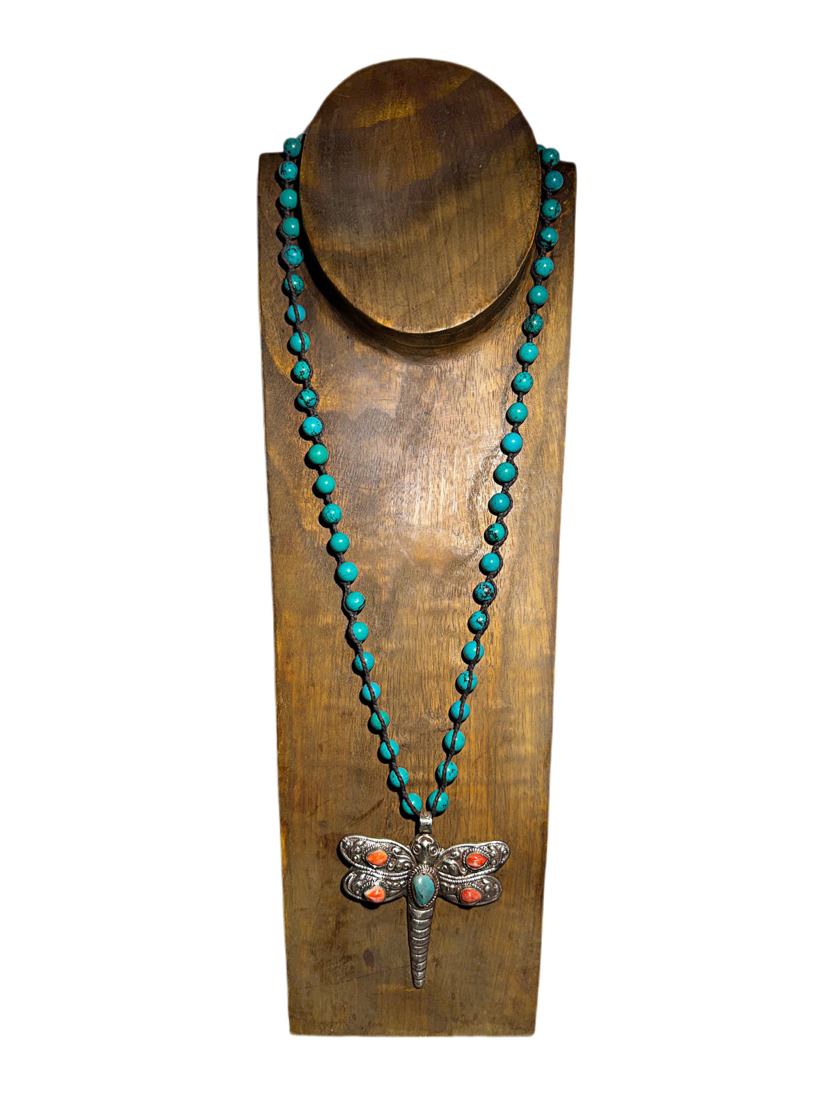 A silver dragonfly pendant  necklace featuring turquoise and coral stones with turquoise beaded chain displayed on a wooden neck stand against a white background.