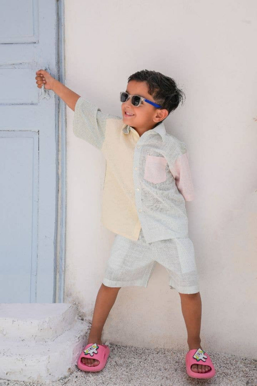 Child wearing sunglasses and a light-colored outfit standing against a white wall.