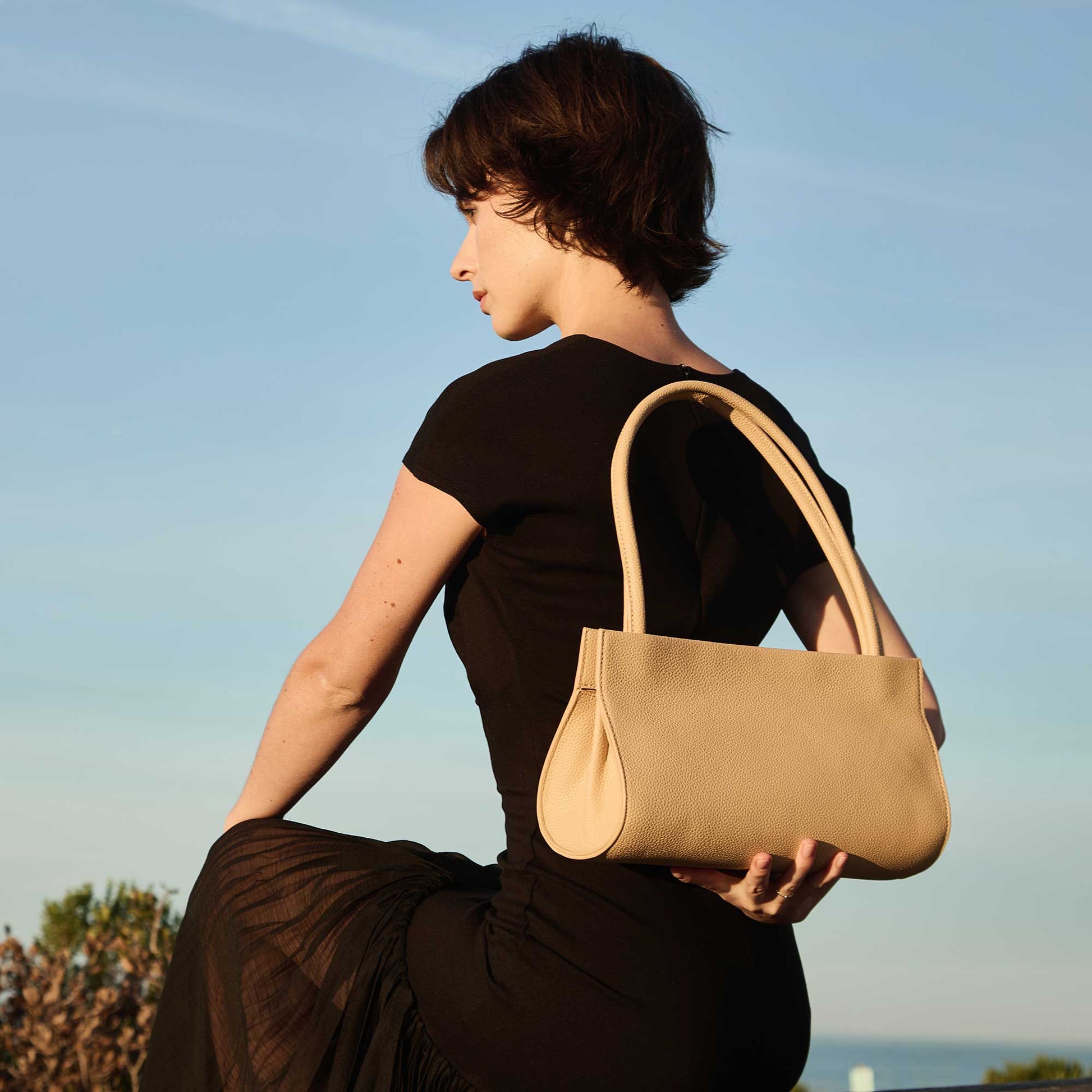 Woman holding a beige handbag against a clear blue sky