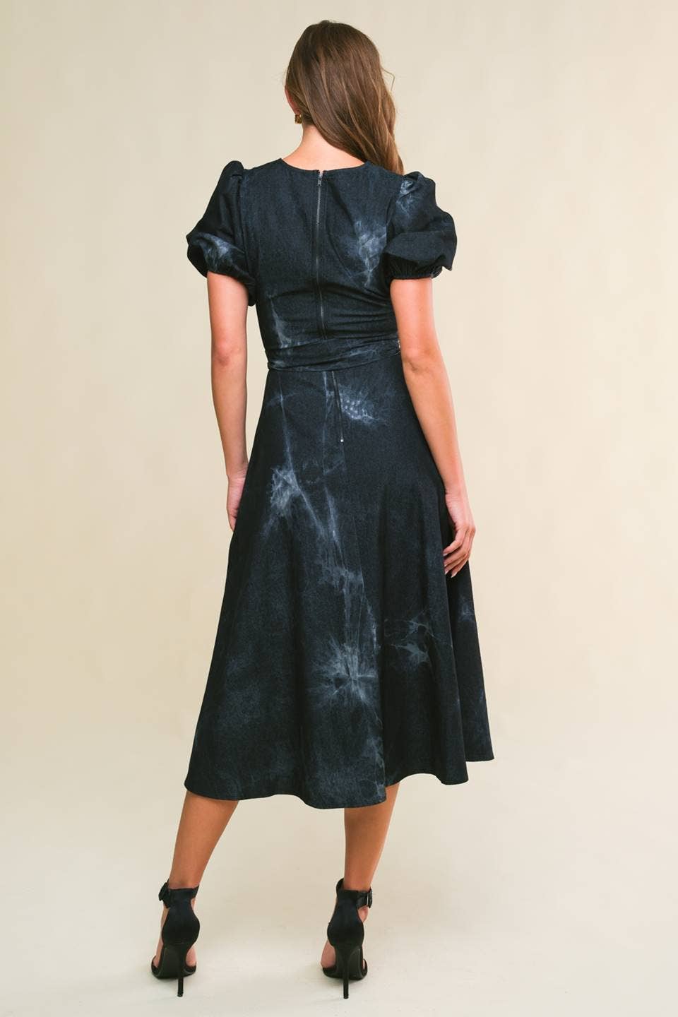 model showing back of twill washed black denim midi dress with round neckline, short puff sleeve, sash tie, full skirt and back zipper closure.