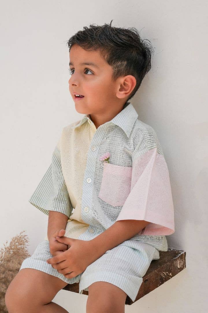 Young boy in a checkered outfit sitting on a wooden block against a plain background