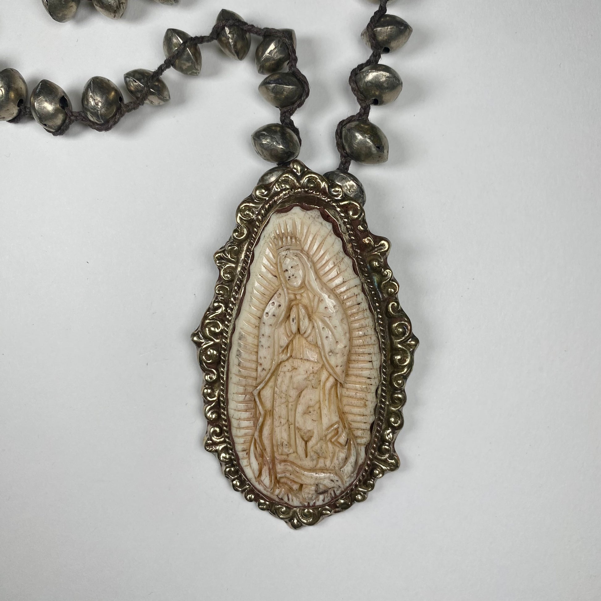 Closeup of Virgen de Guadalupe engraved in Cattle Bone set in  engraved Silver pendant