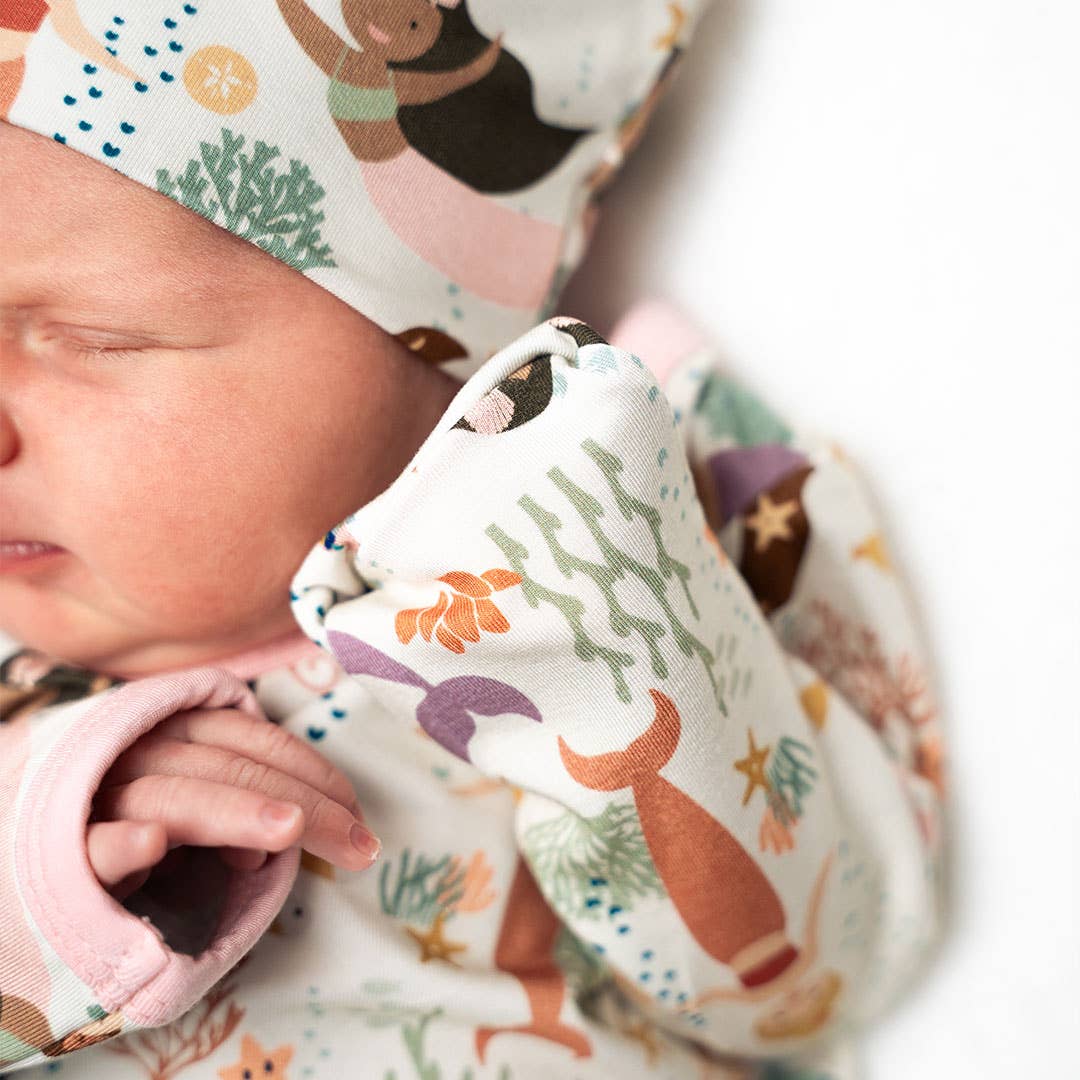 Newborn baby wrapped in a patterned blanket with a hat, featuring animals and nature designs.