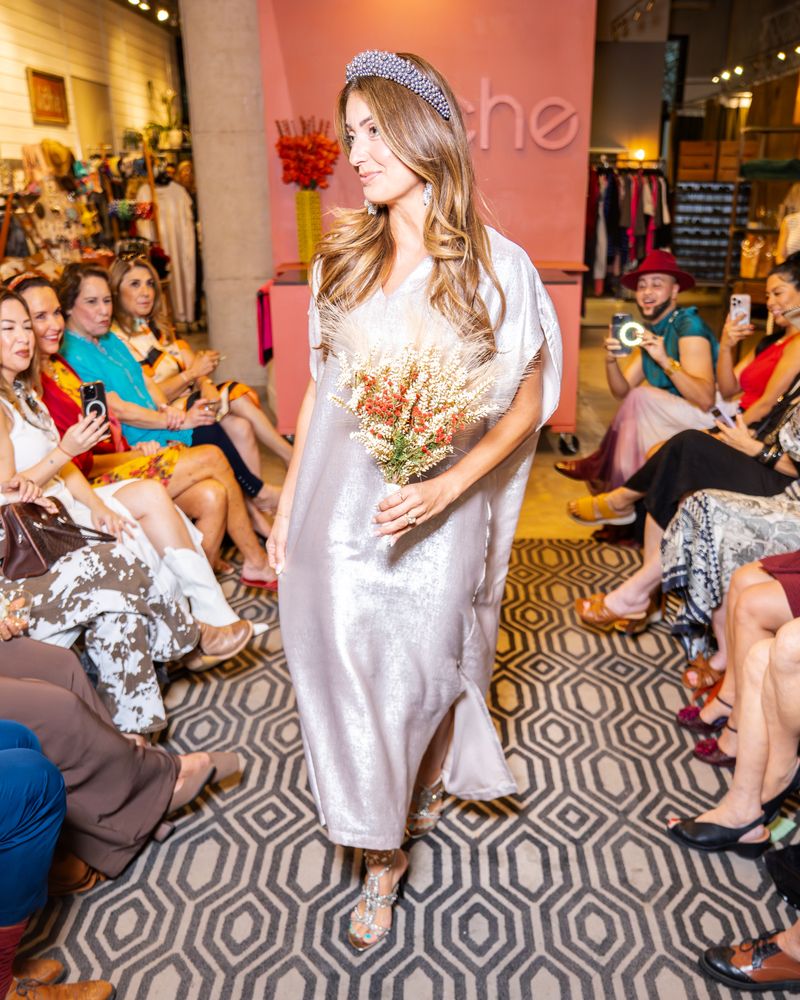 model wearing silver dress, statement earring and headband holding flowers and walking down runway