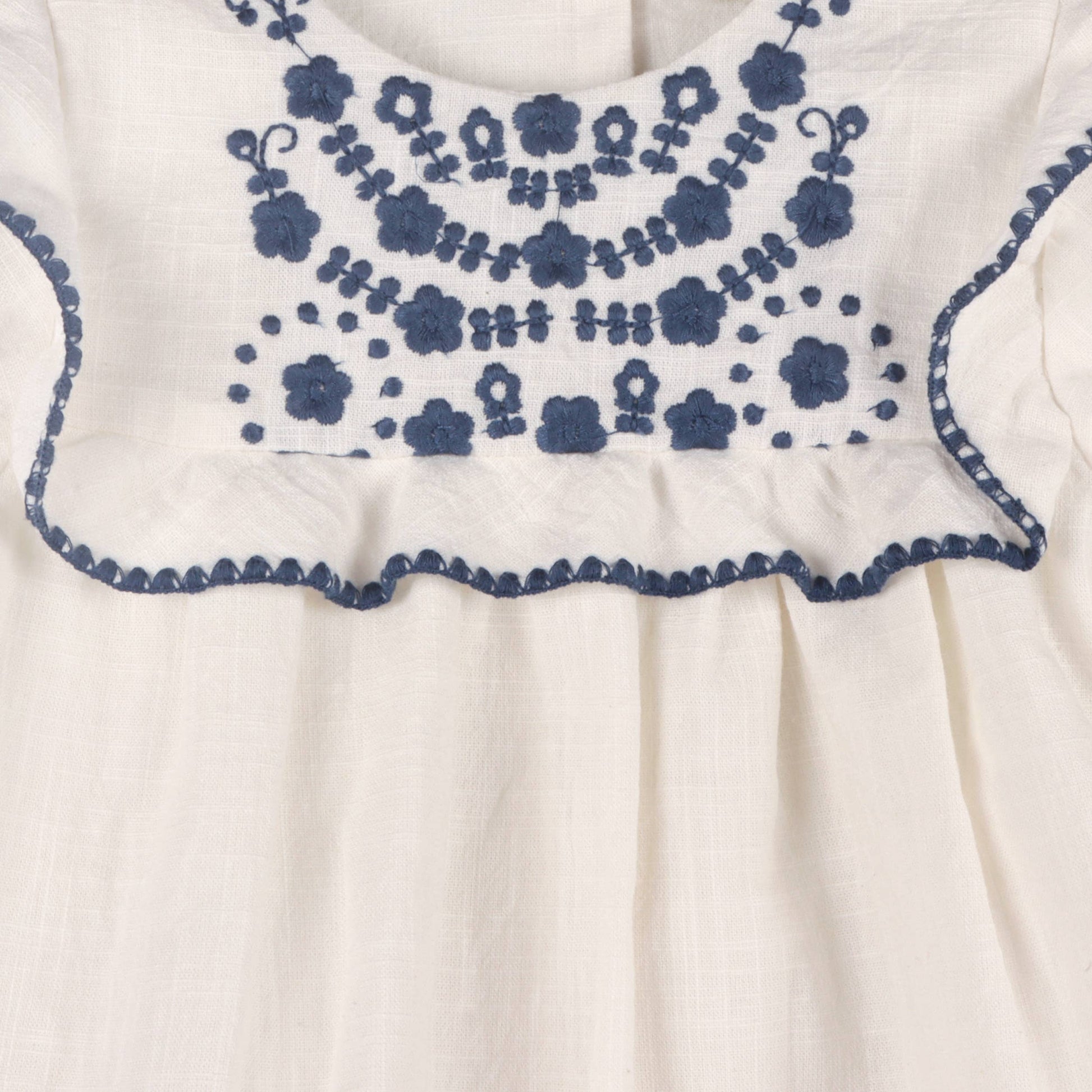 close up of off white baby top with blue floral embroidery design