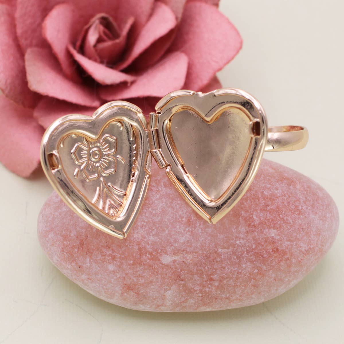 Rose gold heart-shaped locket ring on a pink stone with a pink rose in the background