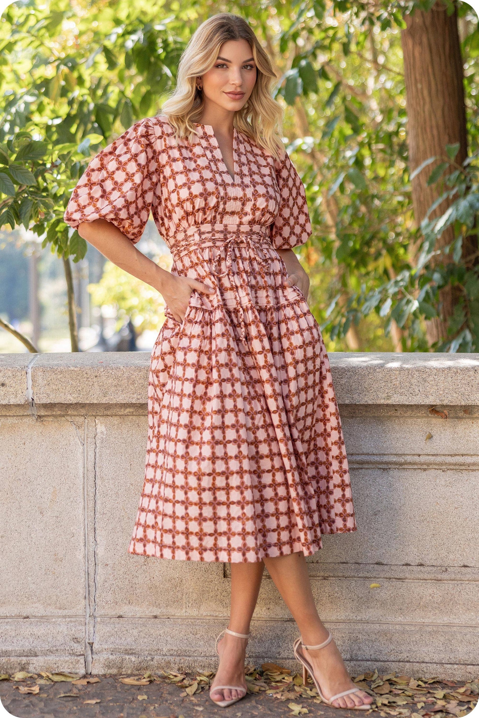 Woman in a red and white patterned dress standing outdoors with greenery in the background