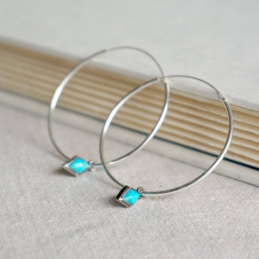 Silver hoop earrings with turquoise square stones on a textured surface