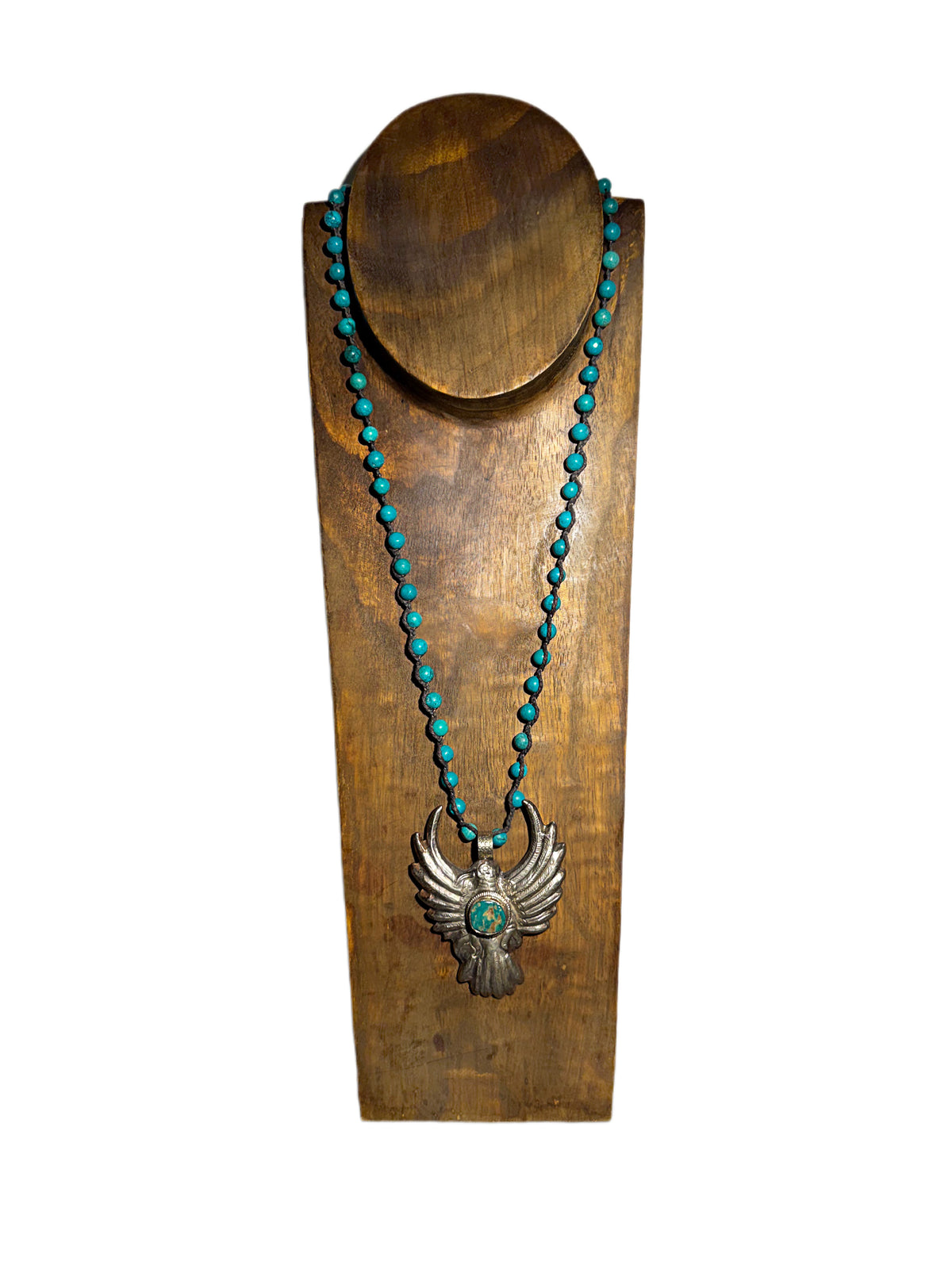 A turquoise and silver necklace displayed on a wooden stand against a white background. The necklace features a series of small turquoise beads and a silver eagle pendant with a turquoise center.