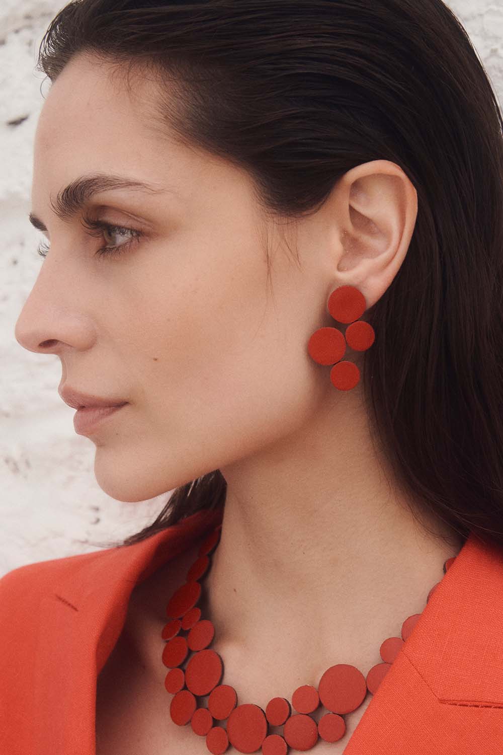 model wearing red circle cluster necklace and earring with red blazer against white rocky background