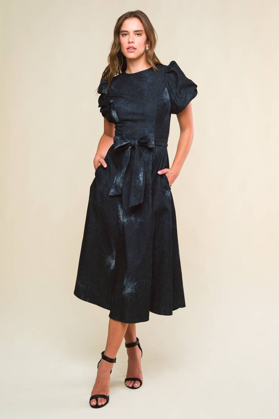 model wearing a twill washed black denim midi dress with round neckline, short puff sleeve, sash tie, full skirt and back zipper closure.