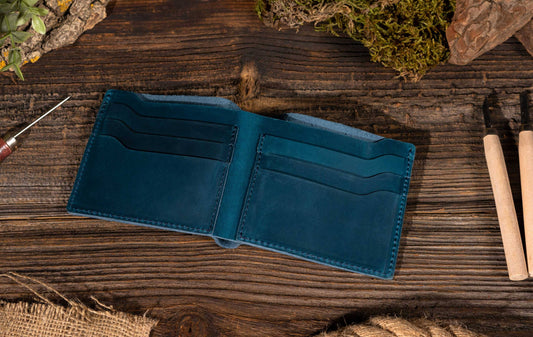 blue leather wallet opened on top of wood surface with tools, rocks and greenery surrounding it