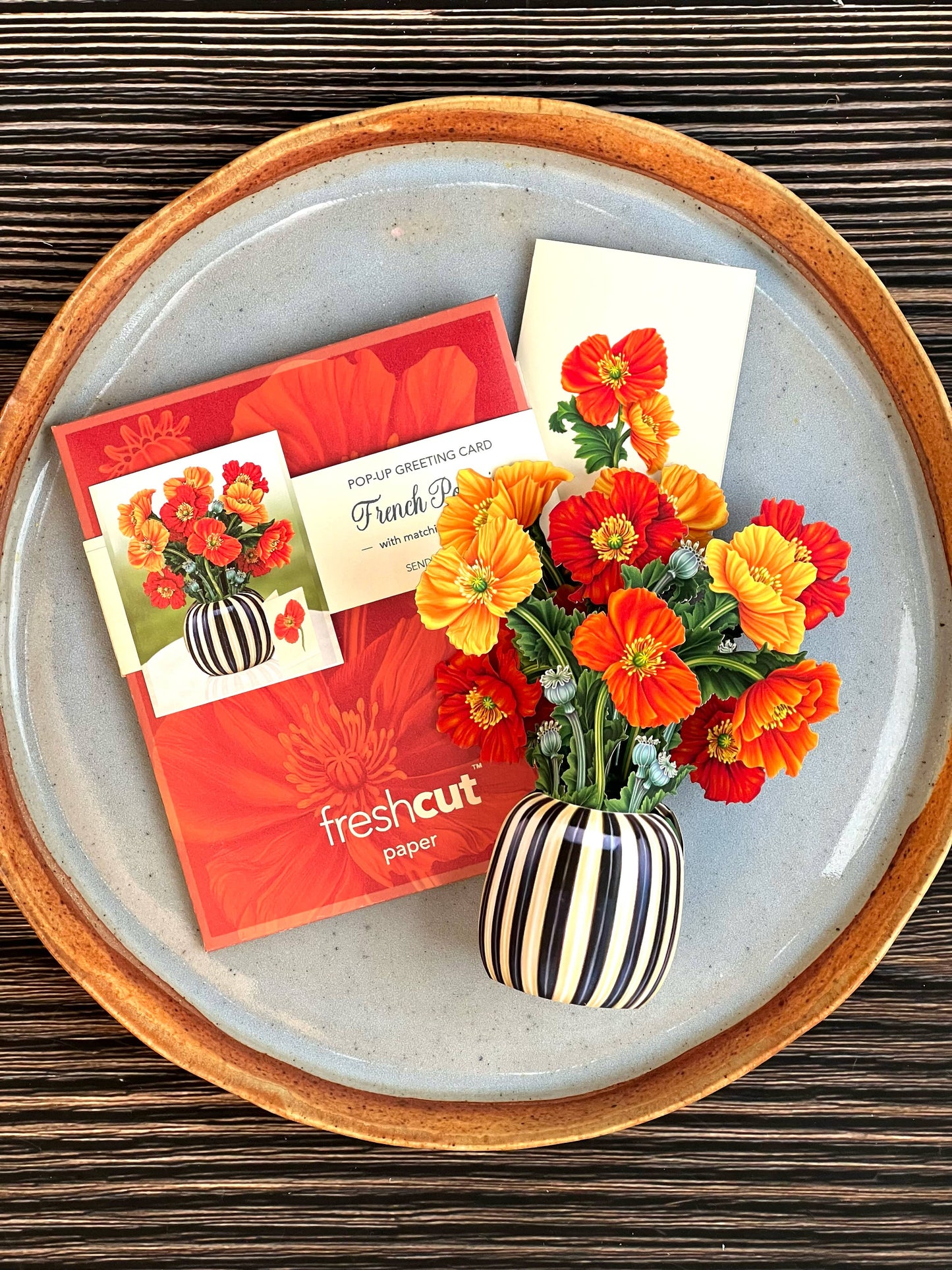 Floral arrangement in a striped vase with 'fresh cut' paper product on a wooden surface