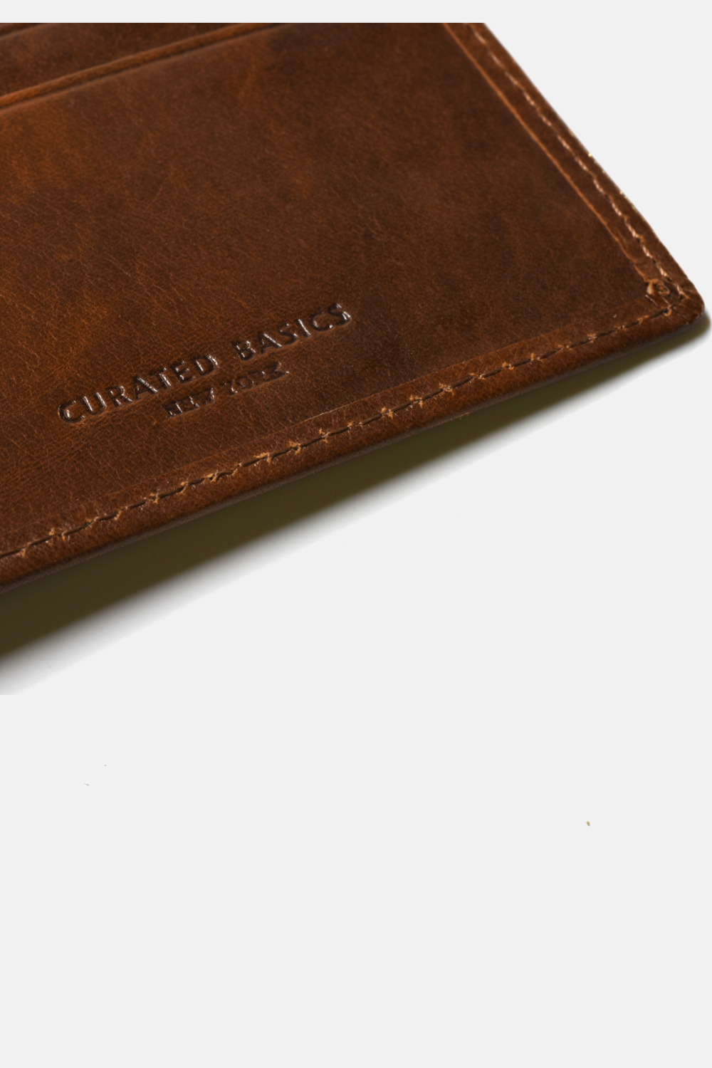 close-up of brown wallet with "curated basics new york" logo